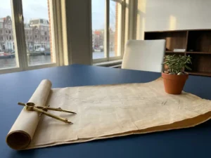 Blueprint unrolling on a modern desk, anchored by a metal compass and green plant, symbolizing structured pipeline planning.
